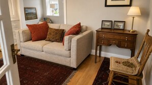 A living room with a beige sofa, a wooden side table with a lamp, a patterned rug, and a chair. - 3 Bed in Giggleswick (oc-c45451) (Settle)