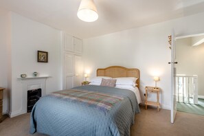 Ein Schlafzimmer mit einem Bett, Nachttischen, einem Kamin und einer Tür zu einem anderen Raum.
