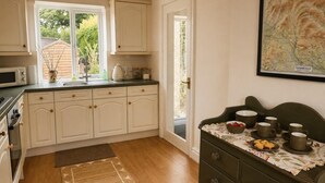 A kitchen with white cabinets, a microwave, a sink, and a dining area with a table set for two. - 3 Bed in Giggleswick (oc-c45451) (Settle)