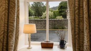 A window with a view of a stone wall and greenery, a lamp, a small wooden box, and a vase with branches. - 3 Bed in Giggleswick (oc-c45451) (Settle)