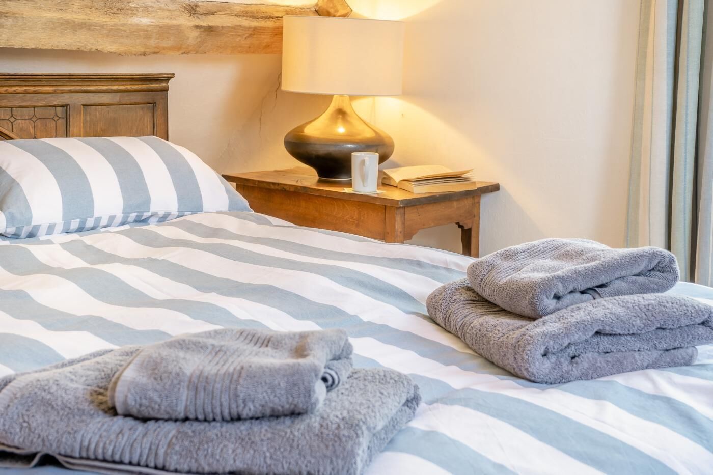 Ein Bett mit gestreifter Bettwäsche, eine Nachttischlampe und ordentlich gefaltete Handtücher.