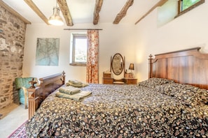 Un dormitorio con una cama grande, un cabecero de madera, una pared de piedra, una ventana con cortinas y un cuadro en la pared.