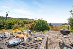 Ein Essbereich im Freien mit Frühstücksangeboten, einem Grill und einem schönen Ausblick.