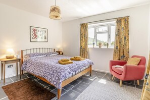 Un dormitorio con cama, lámparas de noche, una silla, una ventana con cortinas y una alfombra.