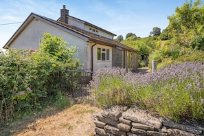 Ett hus med en stenmur, en trädgård med lavendel och en klar himmel.