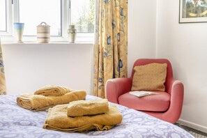 Una habitación con una cama, un sillón rojo con cojín y una ventana con cortinas.