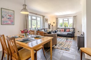 Ein helles Wohnzimmer mit Essbereich, einer Sofagarnitur und einem Kamin.