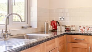 A kitchen with a stainless steel sink, a red kettle, and a coffee maker on the counter. - 3 Bed in Llwyn Du (oc-t44969) (Abergavenny)