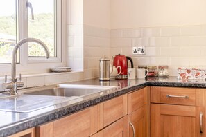 Eine Küche mit einer Spüle aus Edelstahl, einem roten Wasserkocher und einer Kaffeemaschine auf der Arbeitsfläche.