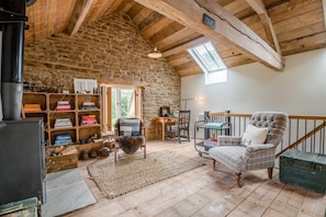 Ein gemütlicher Raum mit Steinwand, Kamin, Bücherregal, bequemen Sesseln und Blick durch eine Dachfenster.