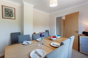 A dining area with a wooden table, grey upholstered chairs, and a vase with purple flowers. - 3 Bed in Croscombe (oc-c45357) (Croscombe)
