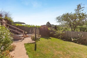 A backyard with a wooden deck, a stone pathway, and a wooden fence. - 3 Bed in Croscombe (oc-c45357) (Croscombe)