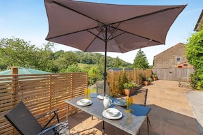Um pátio externo com mesa posta para refeições, um grande guarda-sol e um cercado de madeira.