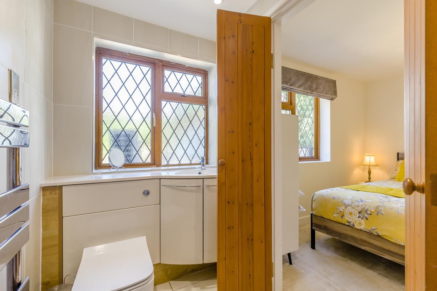 A bedroom with a bed, a bedside table with a lamp, a window with a view, and a wooden door.