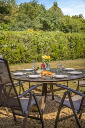 An outdoor dining table set with plates, glasses, a bottle, and a vase with flowers. - 6 Bed in West Wickham (oc-w45418) (Horseheath)