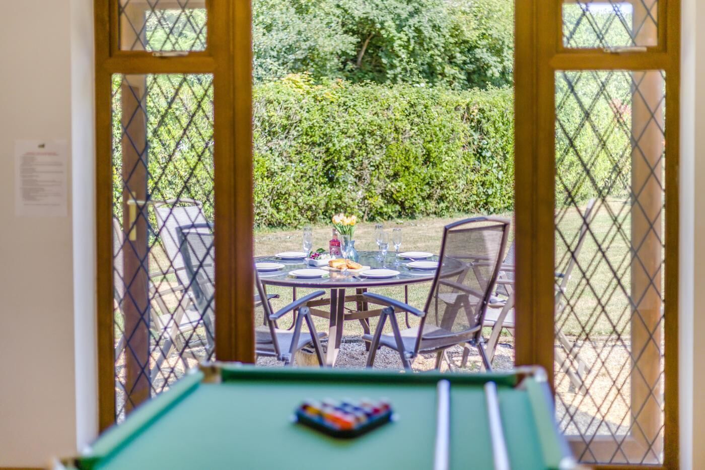 An indoor pool table with a view of an outdoor dining area through a window.