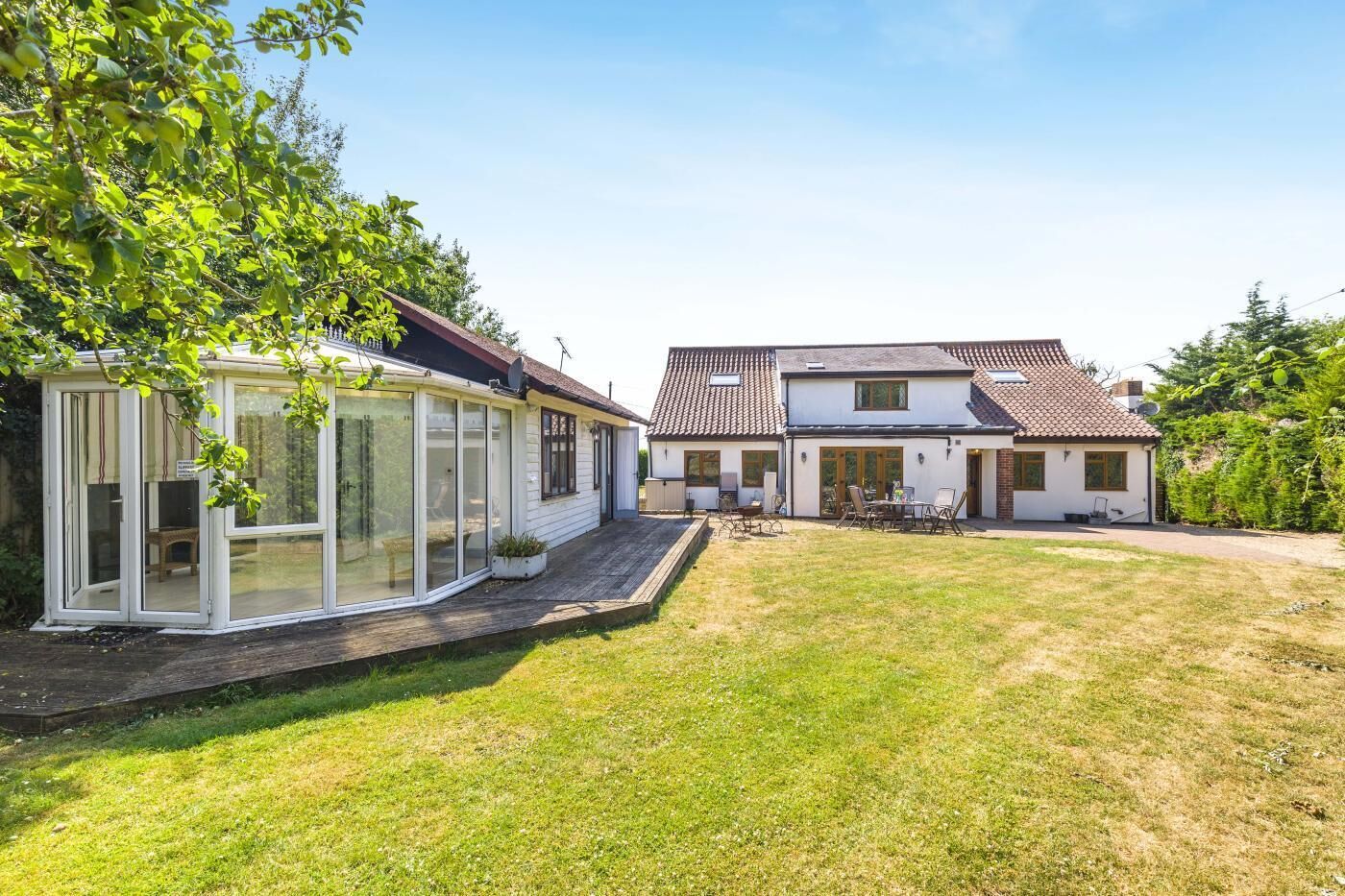 A two-story house with a glass conservatory, a patio with outdoor furniture, and a well-maintained lawn.