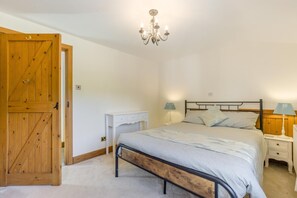 A bedroom with a wooden door, a white bedside table, a bed with a metal frame, two bedside lamps, and a chandelier. - 6 Bed in West Wickham (oc-w45418) (Horseheath)
