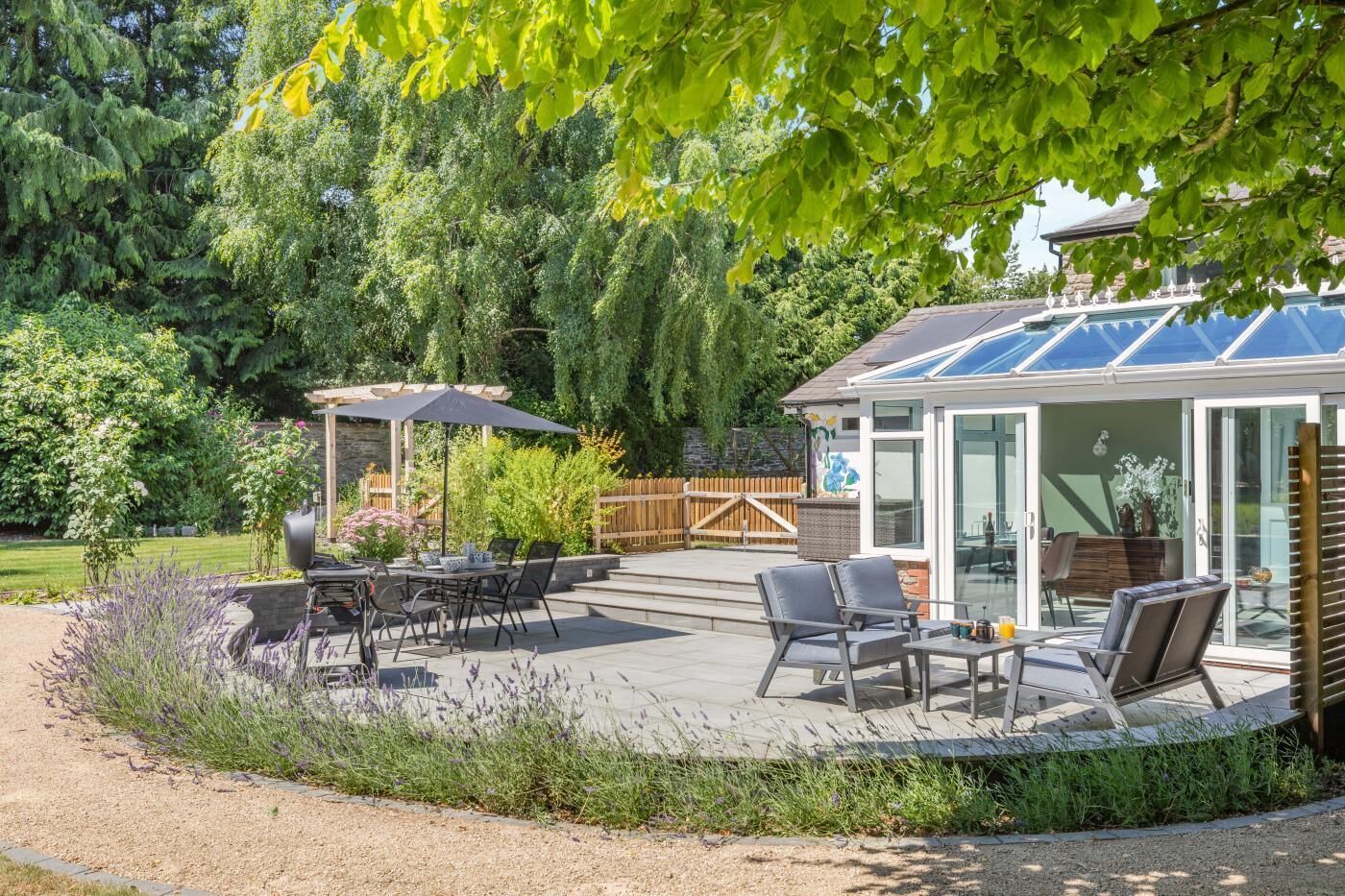 Un espace patio aménagé avec du mobilier d’extérieur, un coin salon couvert et une structure fermée par des parois de verre.