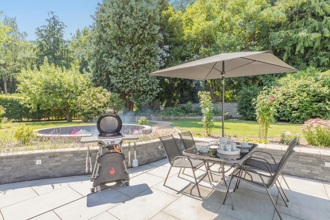 An outdoor patio with a grill, a table with chairs, and an umbrella.