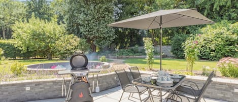 An outdoor patio with a grill, a table with chairs, and an umbrella.