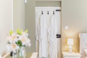 Ein Badezimmer mit weißer Tür, einem Handtuchhalter mit weißen Handtüchern, einem Nachttisch mit Lampe und einer Vase mit Blumen.