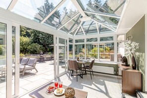 Ein Wintergarten mit Glasdach, einem Esstisch mit Stühlen und Blick auf den Garten.