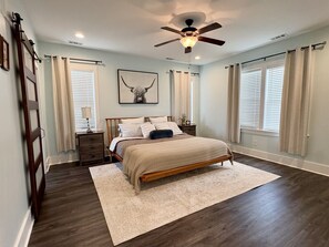 A bedroom with a bed, a nightstand, a ceiling fan, and a window with curtains.