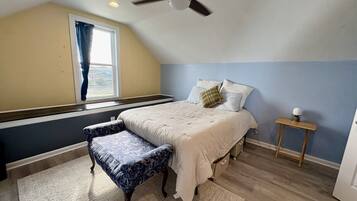 A bedroom with a bed, a bench, a bedside table, a ceiling fan, and a window with curtains.