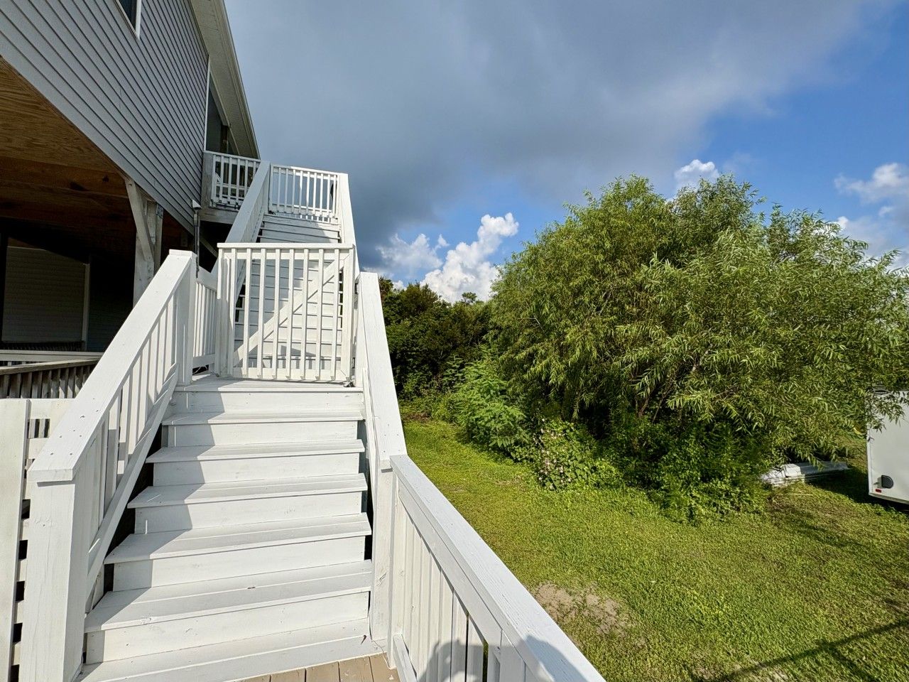 A white staircase leading to a balcony with a view of a green lawn and trees.