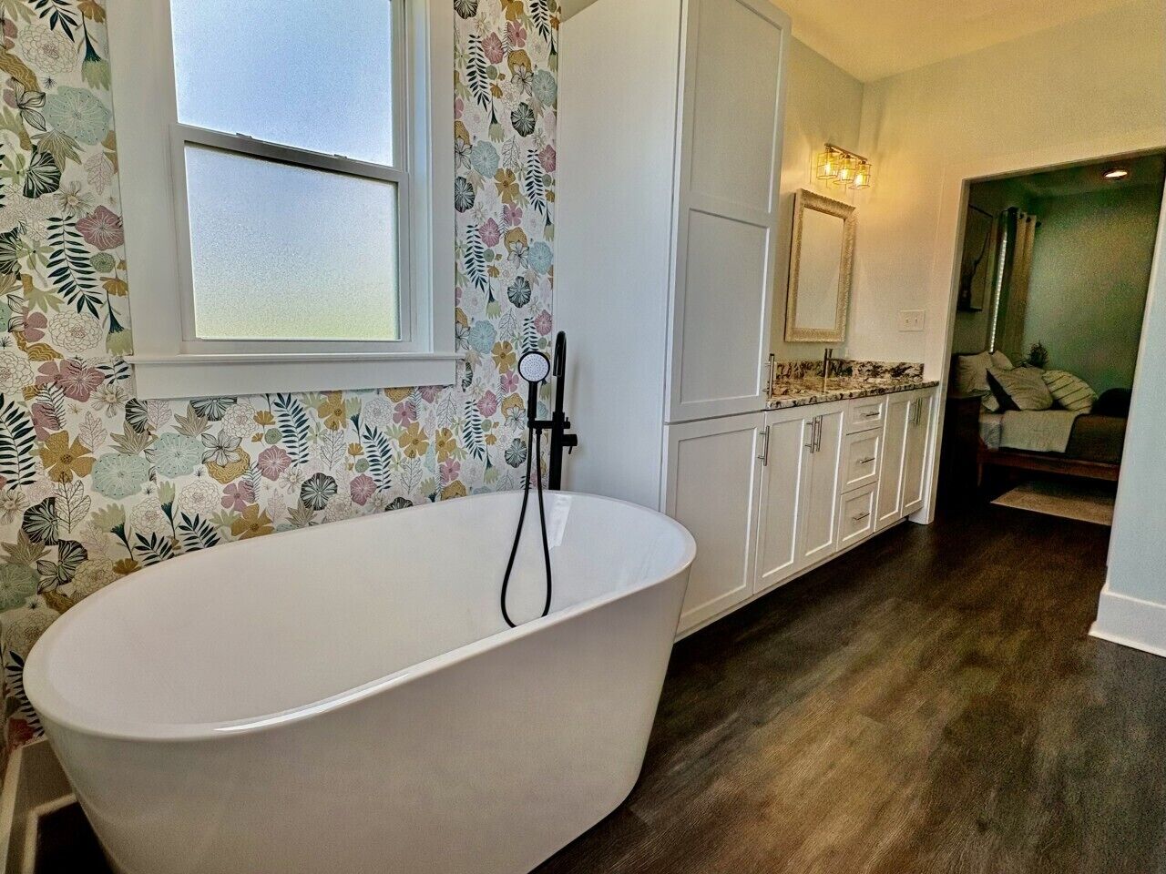 A bathroom with a freestanding bathtub, a window, a mirror, and a cabinet.