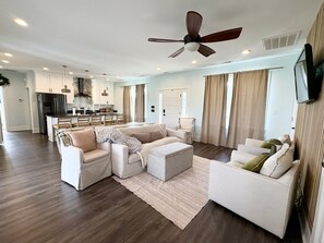 Un salon spacieux comprenant un ensemble de canapés, un pouf et un ventilateur de plafond.