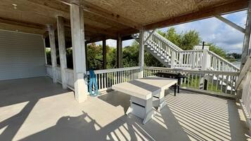 A covered outdoor area with a wooden ceiling, a white railing, and a staircase leading to an upper level.