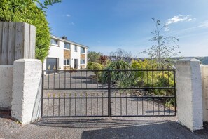 Ein verschlossenes Einfahrtstor zu einem Wohnanwesen mit einer Auffahrt, die zu einem zweistöckigen Haus führt.