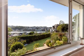Blick aus einem Fenster auf einen gepflegten Garten mit verschiedenen Pflanzen und blauem Himmel.