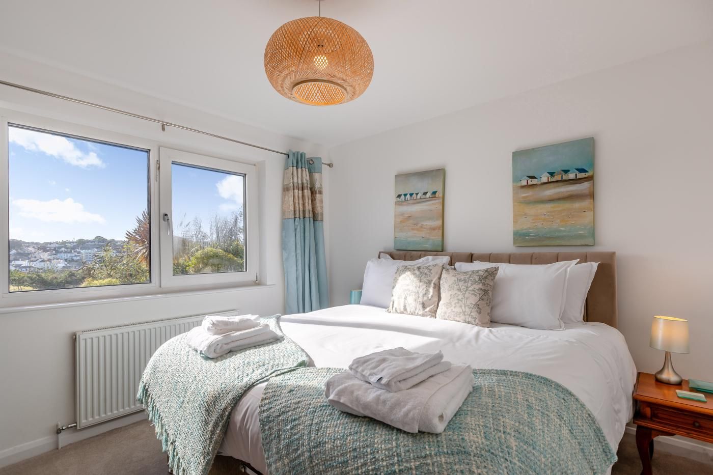 A bedroom with a bed, a window, a radiator, a bedside table with a lamp, and artwork on the wall.