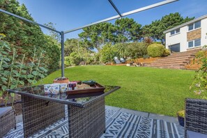 Un espace patio avec une table en verre, des meubles en osier et une pelouse verdoyante.