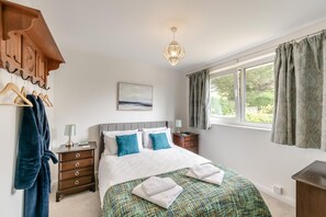 Ein Schlafzimmer mit einem Bett, einem Nachttisch, einer Lampe, einem Kleiderhaken und einem Fenster mit Vorhängen.