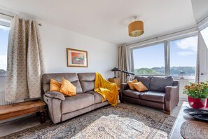 Ein Wohnzimmer mit zwei Sofas, einem gemusterten Teppich, einem Gemälde und Blick durch große Fenster.