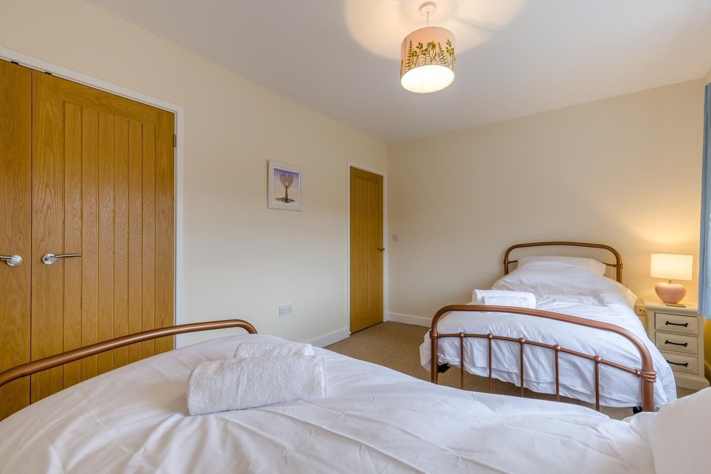 A bedroom with two single beds, a wooden wardrobe, a bedside table with a lamp, and a ceiling light fixture.