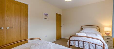 Um quarto com duas camas de solteiro, um guarda-roupa de madeira, uma mesa de cabeceira com uma lâmpada e um lustre.