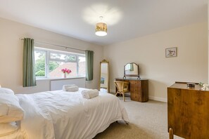 A bedroom with a bed, a dresser, a chair, a mirror, and a window with curtains. - 2 Bed in Heacham (oc-l44862) (Heacham)