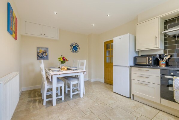 A compact kitchen with a dining table set for two, a refrigerator, microwave, and a small cabinet. - 2 Bed in Heacham (oc-l44862) (Heacham)