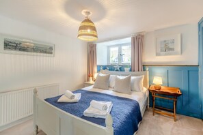 Quarto de hotel com cama, mesa de cabeceira, luminária, janela com cortinas e um quadro na parede.