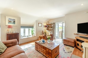 Ein Wohnzimmer mit Sofa, Couchtisch, Fernseher und einer Schiebetür zu einem Balkon.