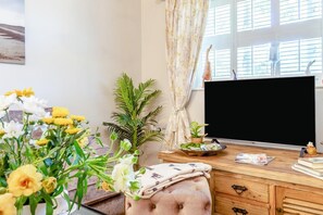 Ein Zimmer mit einem Holztisch, einem Fernseher, einem Fenster mit Vorhängen und mehreren Pflanzen.