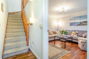 Eine Treppe mit Teppichstufen und Holzwerteln, ein Wohnzimmer mit Sofa, Couchtisch und Teppich, sowie ein Bild an der Wand.