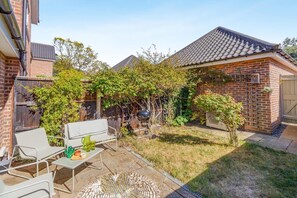Ein Garten mit Terrasse, Grill und einem Haus mit Backsteinfassade.