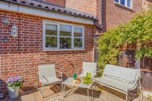 A brick house with a window, a patio with two chairs and a table, and a potted plant. - 2 Bed in Westleton (oc-w42586) (Westleton)