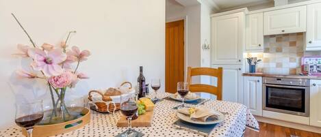 Un coin repas avec une table dressée pour deux personnes, agrémentée d’une nappe à pois, d’un vase de fleurs, d’une bouteille de vin et d’un panier de pain.